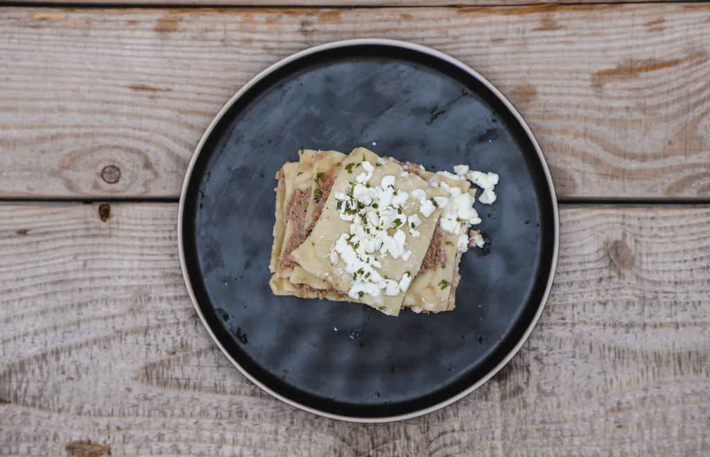 lasagne pour chiens sur un decor de bois sur une assiette noire avc du fromage de cottage et du persil et viande hachee